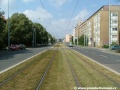 Zatravněný přímý úsek tramvajové tratě na zvýšeném tělese ve středu Černokostelecké ulice míří k úrovňovému přejezdu pro automobily.