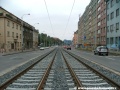 Středem Plzeňské ulice na zvýšeném tělese pokračuje tramvajová trať v klesání.