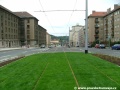 Zvýšené těleso tramvajové tratě ve středu Podbabské ulice s asfaltovým krytem kolejiště.